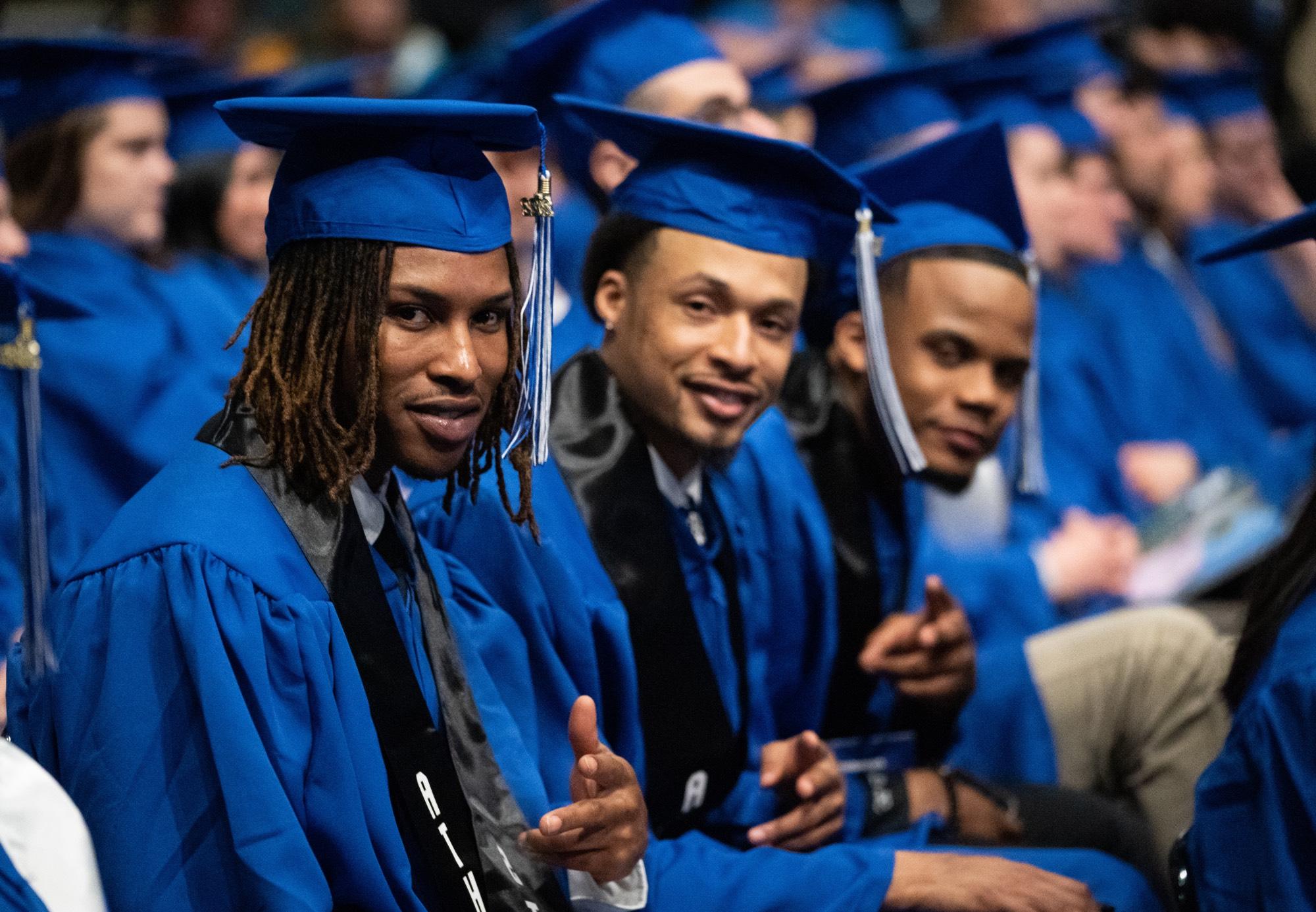 students smiling and pointing at camera at commencement